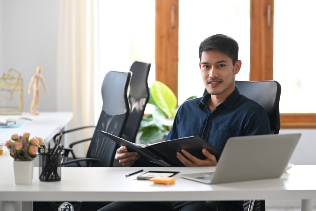 Confident investment adviser sitting in modern office and smiling to camera.