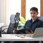 Confident investment adviser sitting in modern office and smiling to camera.