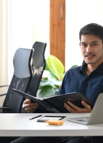 Confident investment adviser sitting in modern office and smiling to camera.