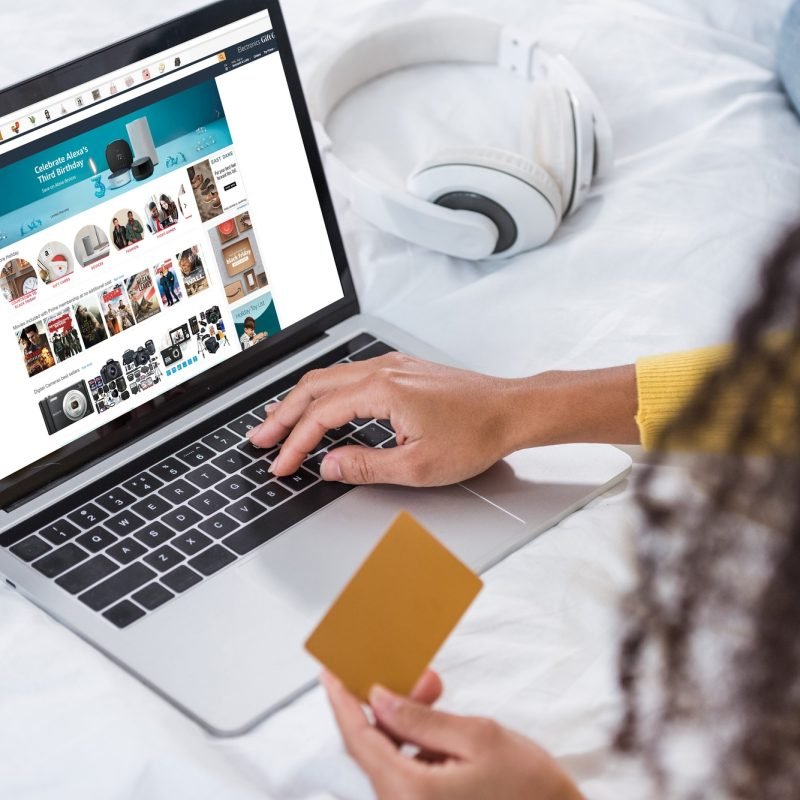 cropped image of woman holding credit card and using laptop with amazon on screen